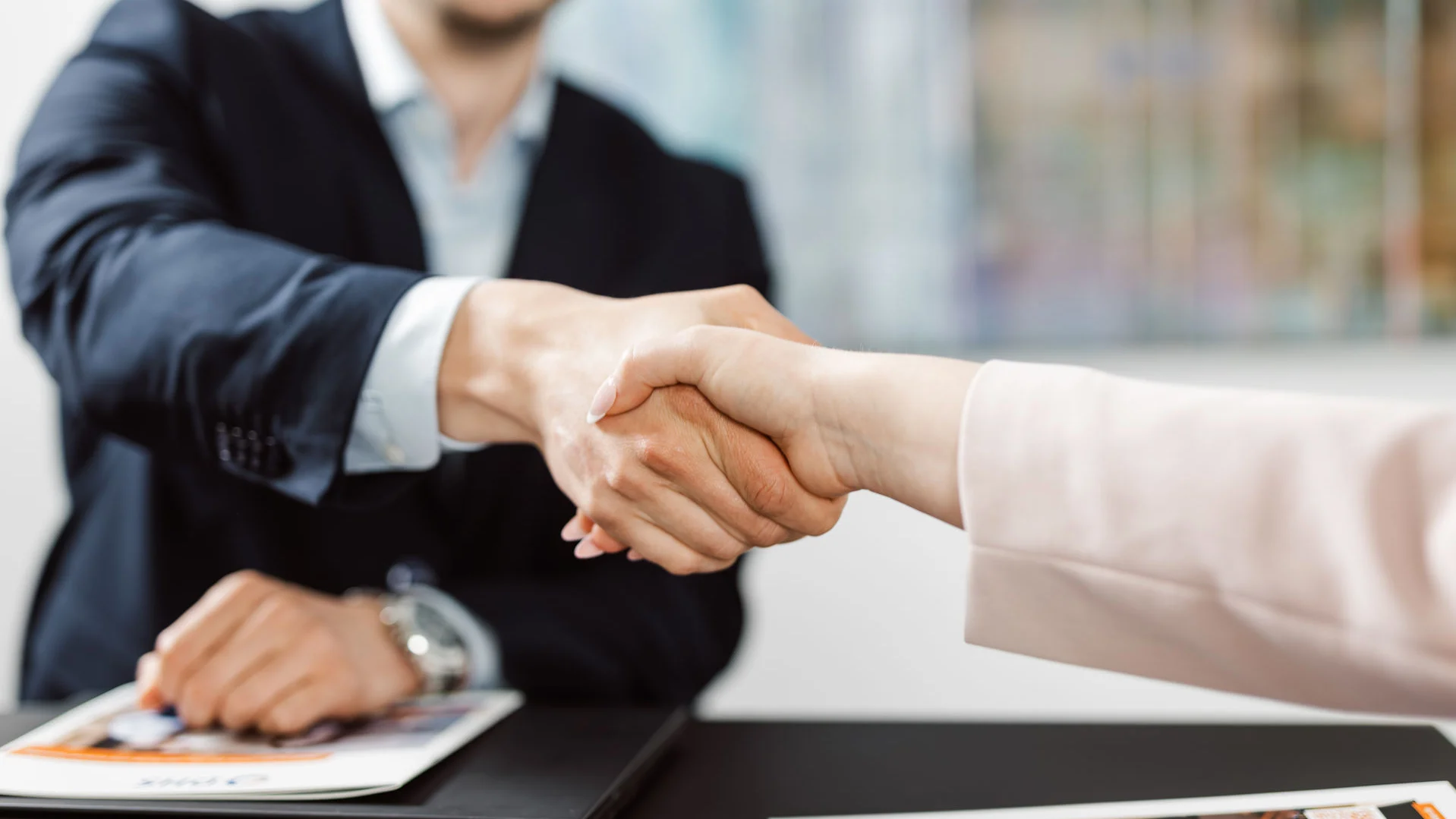 Zwei Personen in Businesskleidung geben sich die Hand, man erkennt keine Gesichter