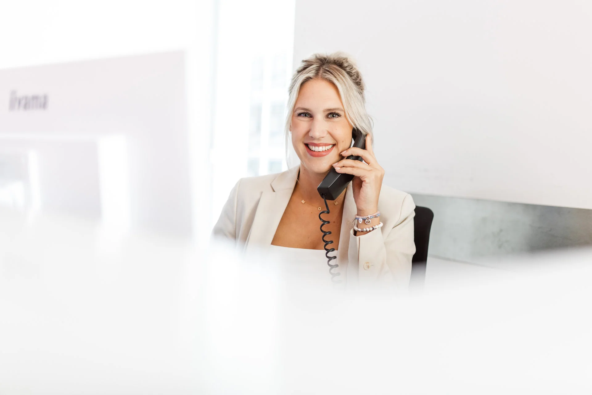 Lächelnde blonde Frau am Empfang spricht am Telefon in einem hellen Büro