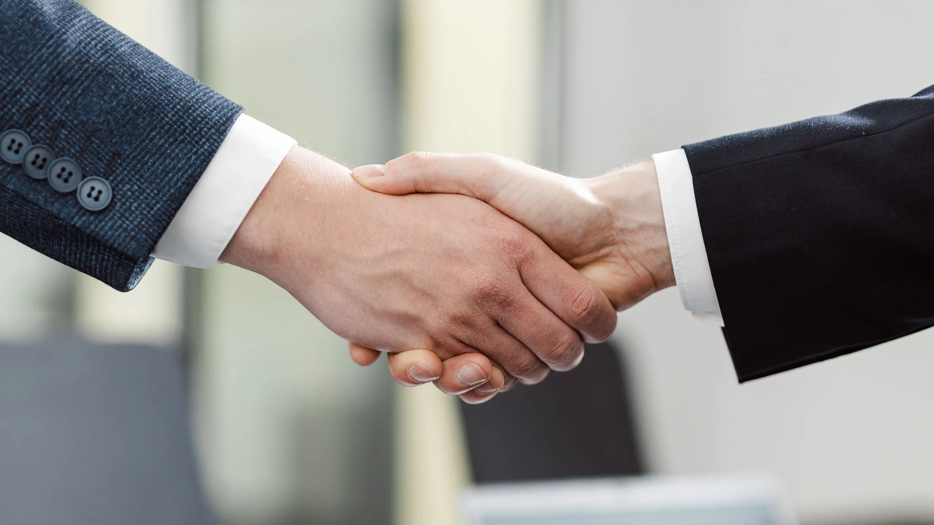 zwei Händen greifen ineinander zum Handshake, man sieht die Ärmel zweier Anzüge.