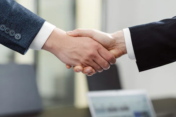 zwei Händen greifen ineinander zum Handshake, man sieht die Ärmel zweier Anzüge.