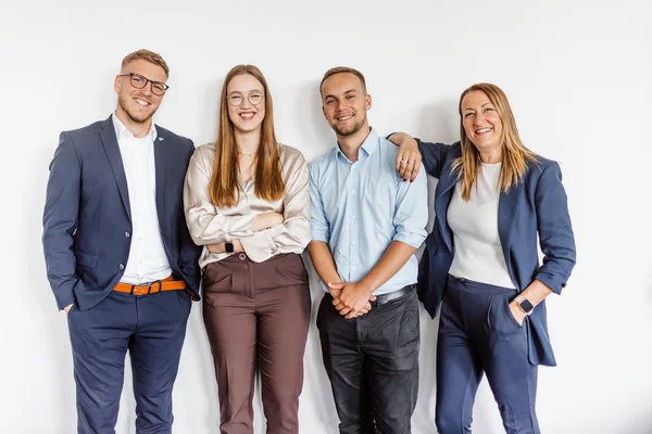 zwei Männer und zwei Frauen in Businesskleidung stehen eng zusammen und lächeln in die Kamera