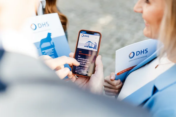 Hand hält Smartphone auf dem die Webseite von DHS Versicherungsmakler geöffnet ist