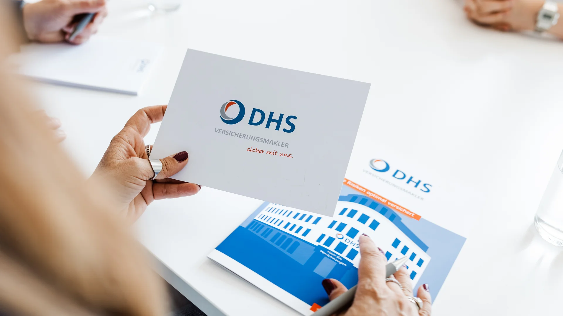 Über Schulter Fotografie, man sieht eine hand die eine Moderationskarte hält wo das Logo von DHS Versicherungsmakler drauf ist