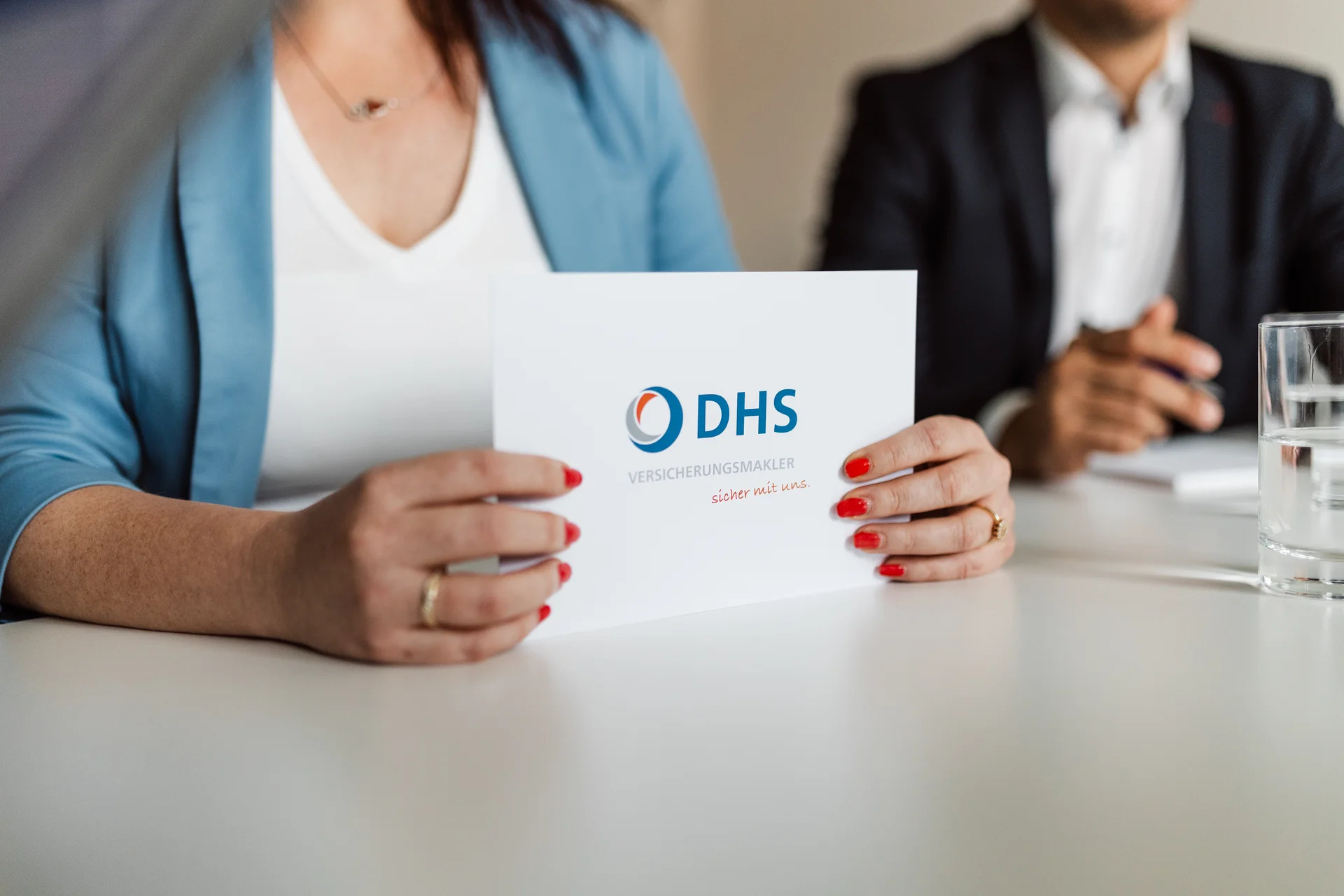 Frau hält eine Karte mit dem DHS Versicherungsvermittler-Logo und dem Slogan 'sicher mit uns'