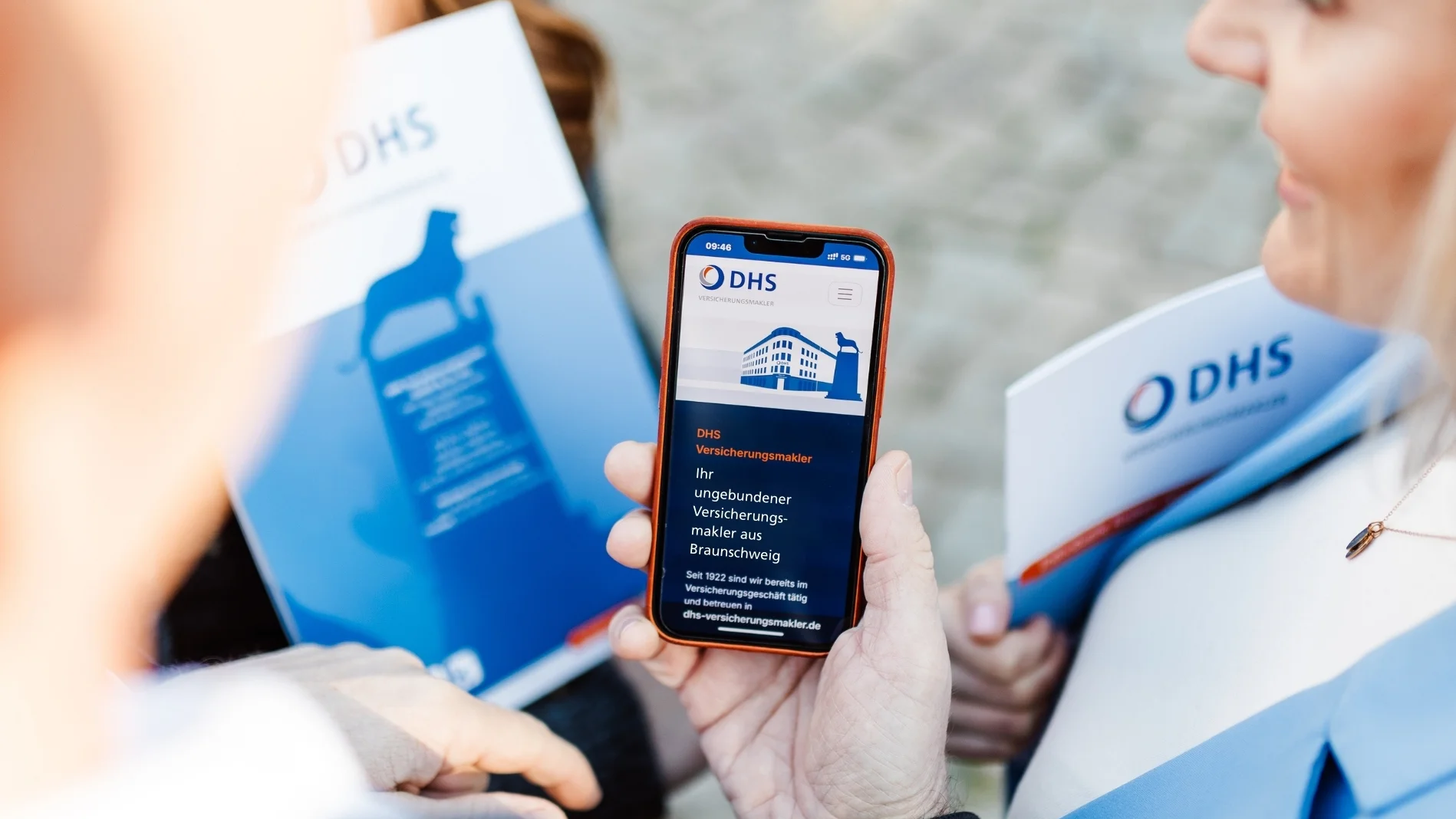 Hand hält Smartphone, auf der die Webseite von DHS Versicherungsmakler zu sehen ist