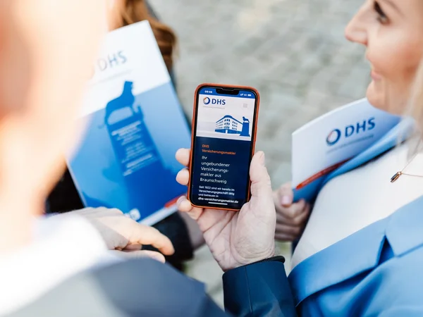 Hand hält Smartphone, auf der die Webseite von DHS Versicherungsmakler zu sehen ist