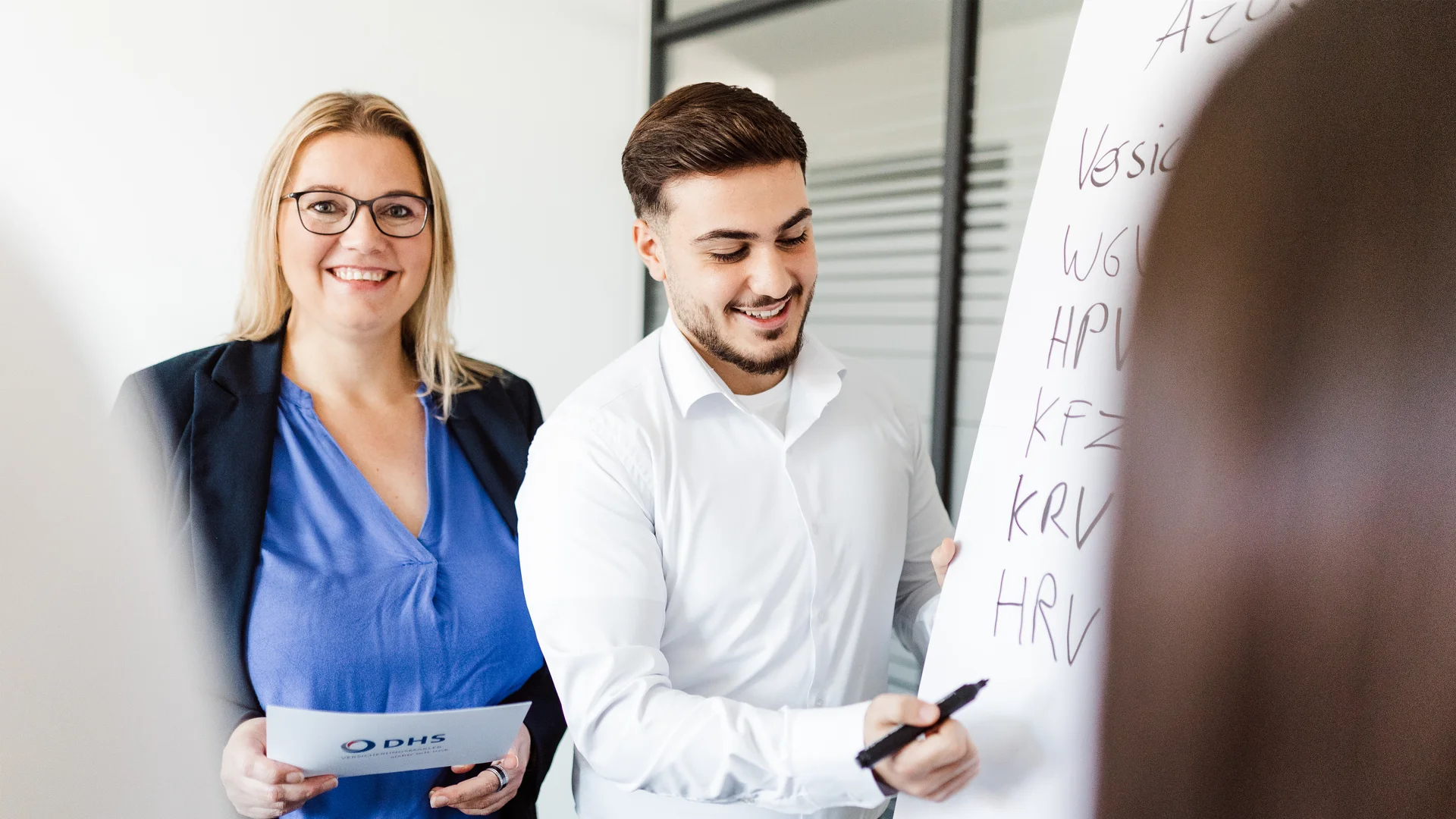 Frau in Businesskleidung steht neben männlichem Azubi an einem Fliphart