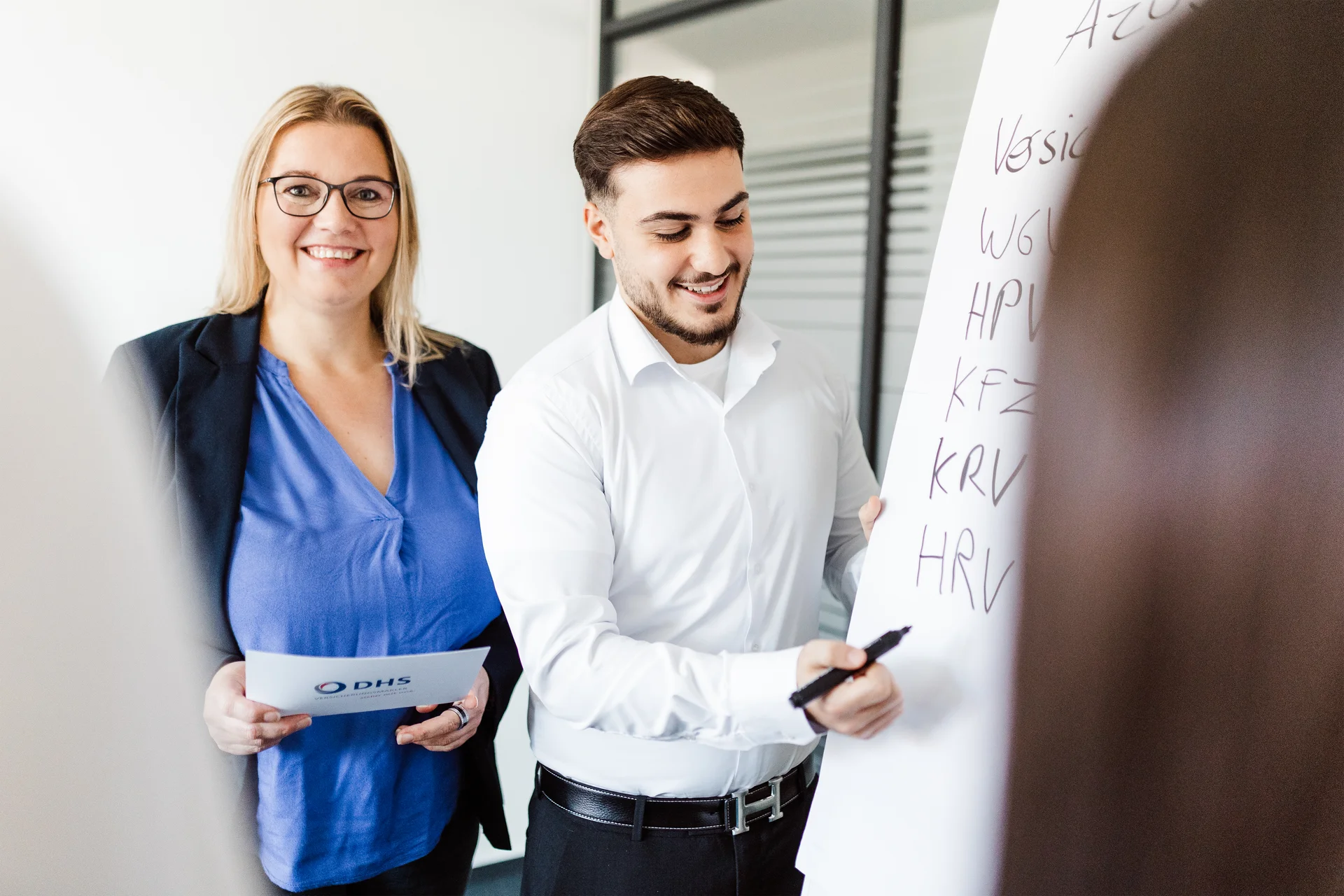 Eine Ausbilderin in Businesskleidung steht mit einem Auszubildenden an einem Flipchart